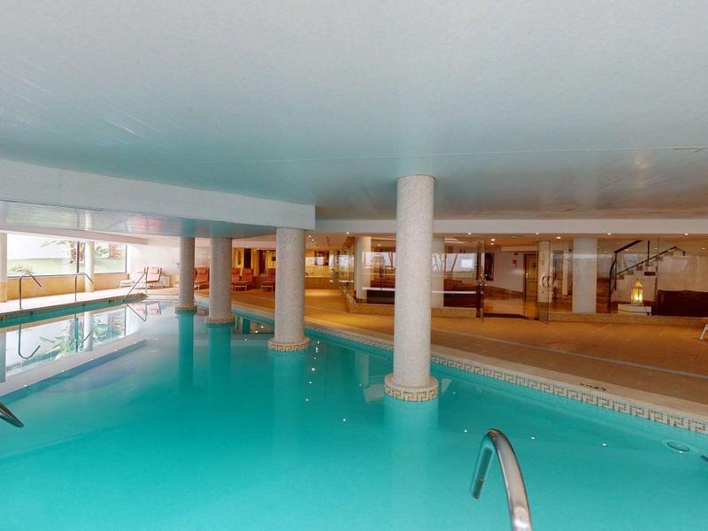 Hotelowy basen kryty z czystą wodą, białe kolumny i strefa wypoczynkowa w tle.