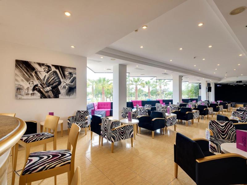 Przestronny hotelowy salon z czarnymi i zebrastymi krzesłami oraz dużymi oknami z widokiem na zieleń.