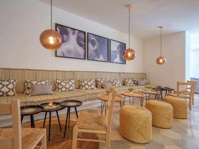 Lounge d'hotel moderno con sedie in legno, tavoli rotondi e sgabelli gialli sotto lampade di rame.