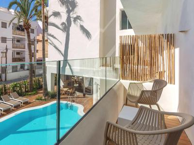 Balcone con due sedie e ringhiera in vetro con vista su piscina e palme.