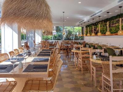 Ristorante luminoso e moderno con sedie di legno, decorazioni verdi e luce naturale.