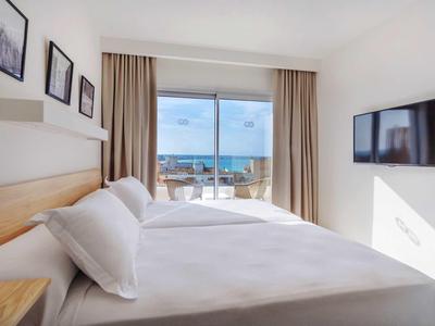 Camera d'hotel luminosa con letto matrimoniale, vista mare e TV a parete