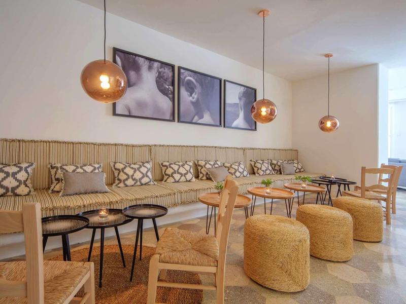 Lounge d'hotel moderno con sedie in legno, tavoli rotondi e sgabelli gialli sotto lampade di rame.