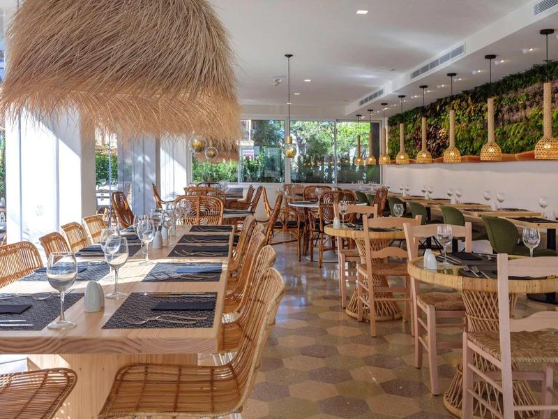 Ristorante luminoso e moderno con sedie di legno, decorazioni verdi e luce naturale.