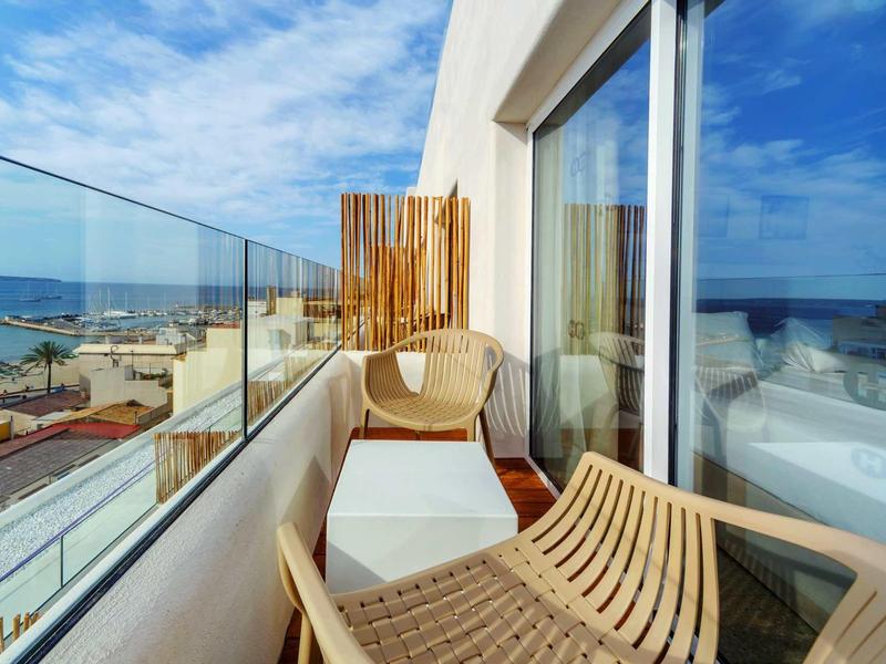 Balcone con parapetto in vetro, sedie e vista sul mare e sulla spiaggia.