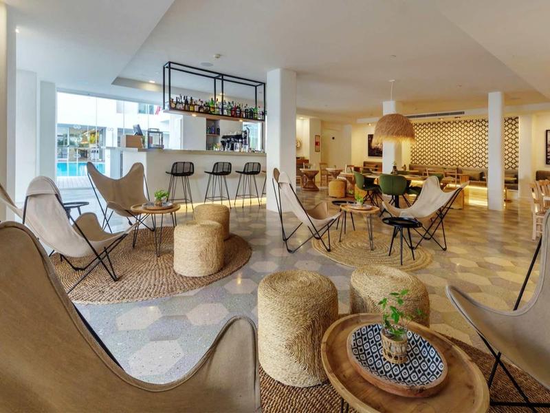 Lounge dell'hotel moderna e luminosa con poltrone accoglienti e tavoli dai toni caldi.