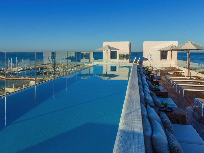 Piscina sul tetto con vista sulla città e lettini prendisole sotto ombrelloni.