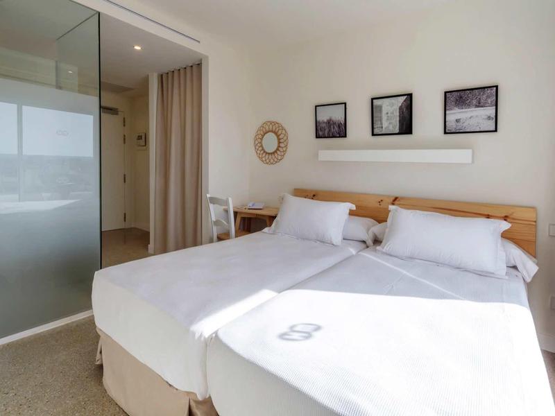 Camera luminosa con letto matrimoniale, testiera in legno e porte scorrevoli in vetro smerigliato.