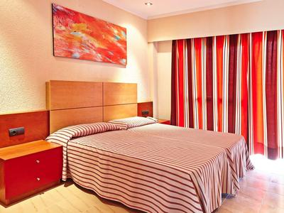 Camera d'hotel con letto matrimoniale, comodino rosso e tende a righe rosse.