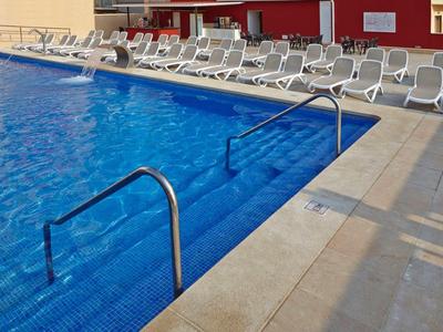 Großer blauer Pool mit Edelstahlgeländern und weißen Liegestühlen auf hellem Boden.