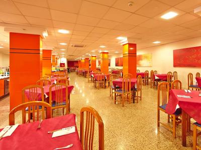 Ampia sala da pranzo con tavoli rossi e sedie di legno.