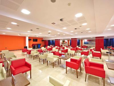 Ampia sala da pranzo con sedie rosse e crema e tavoli, soffitto luminoso e illuminazione.