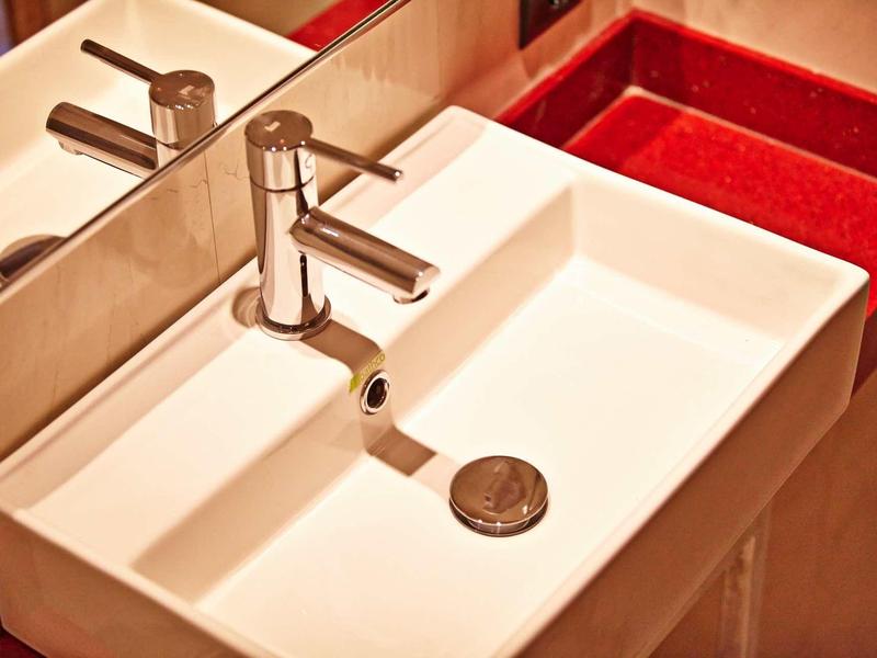 Lavabo bianco moderno con rubinetto cromato in bagno con dettagli rossi.