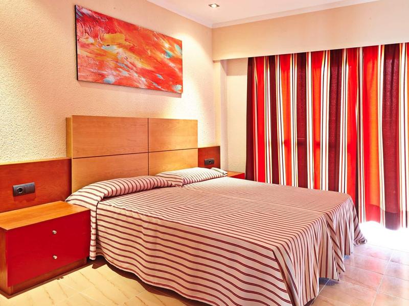 Camera d'hotel con letto matrimoniale, tende a righe rosse e quadro astratto.