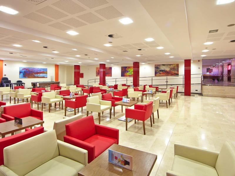 Ampio salone con poltrone rosse e beige in un hotel moderno.