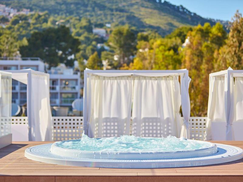 Hot tub on a terrace with white curtains and green landscape in the background.
