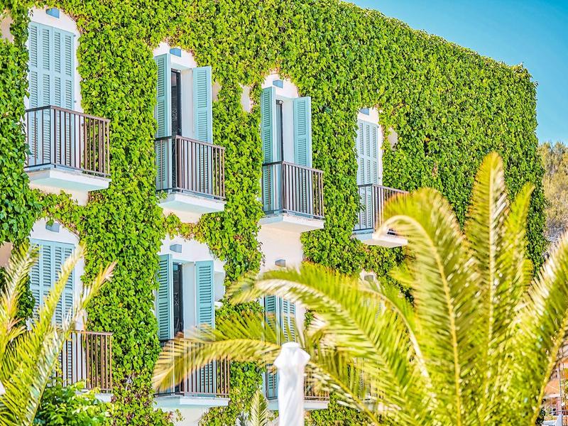 Facade of a hotel covered with green ivy and balconies under a blue sky