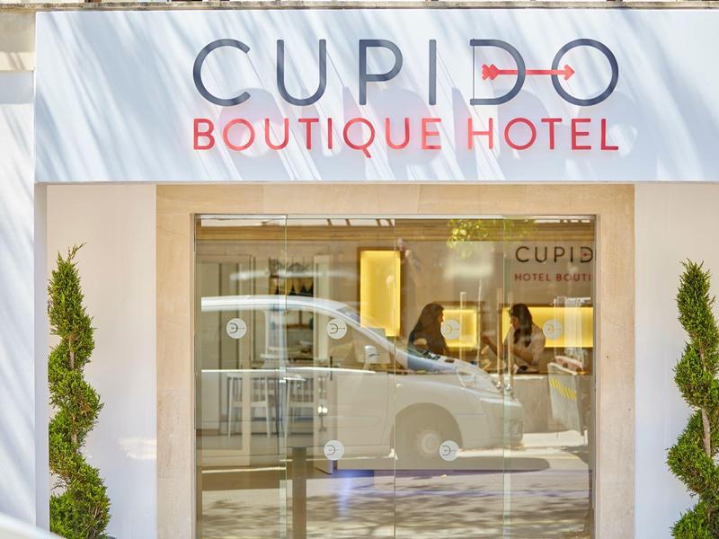 Facade of Cupid Boutique Hotel with glass door and car reflection.