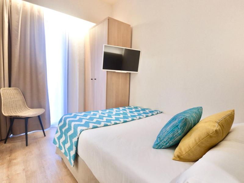 Modern hotel room with double bed, chair, TV, and daylight from large window.