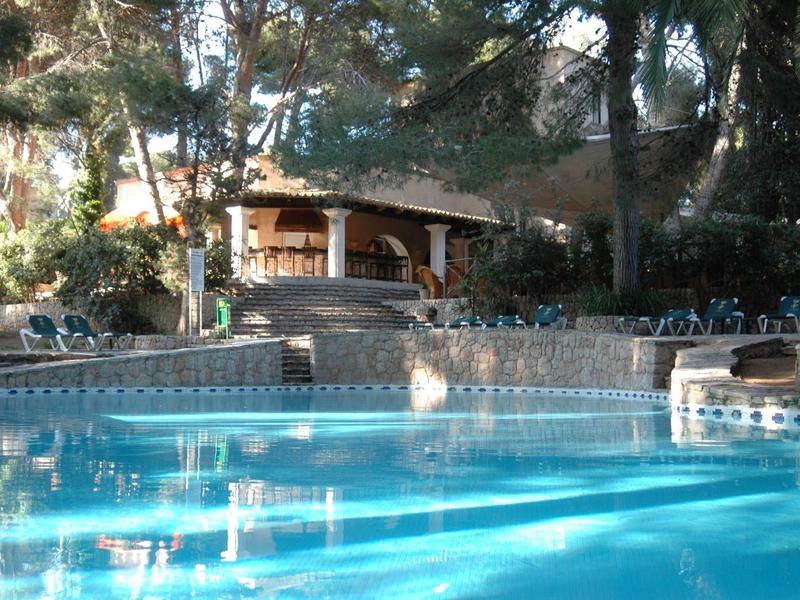 Clear water swimming pool in front of a wooden pavilion in a wooded hotel area.