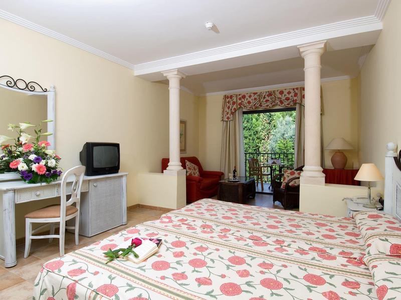 Bright hotel room with double bed, desk, TV, and garden view through glass doors