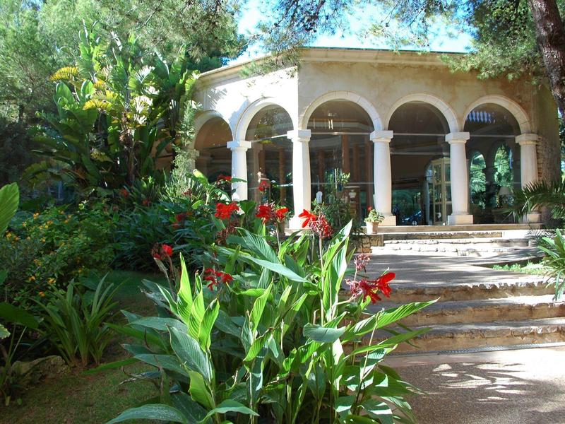 A garden with blooming plants in front of a building with arches and glass windows.