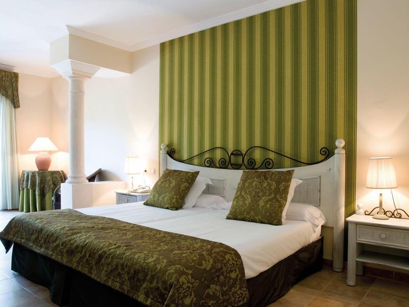 Modern hotel room with large bed, green wall, and bedside tables with lamps.