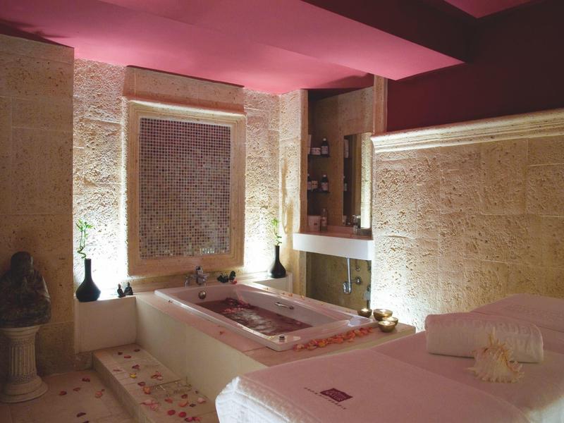 Calm spa room with massage table, bathtub, and soft lighting for relaxation.