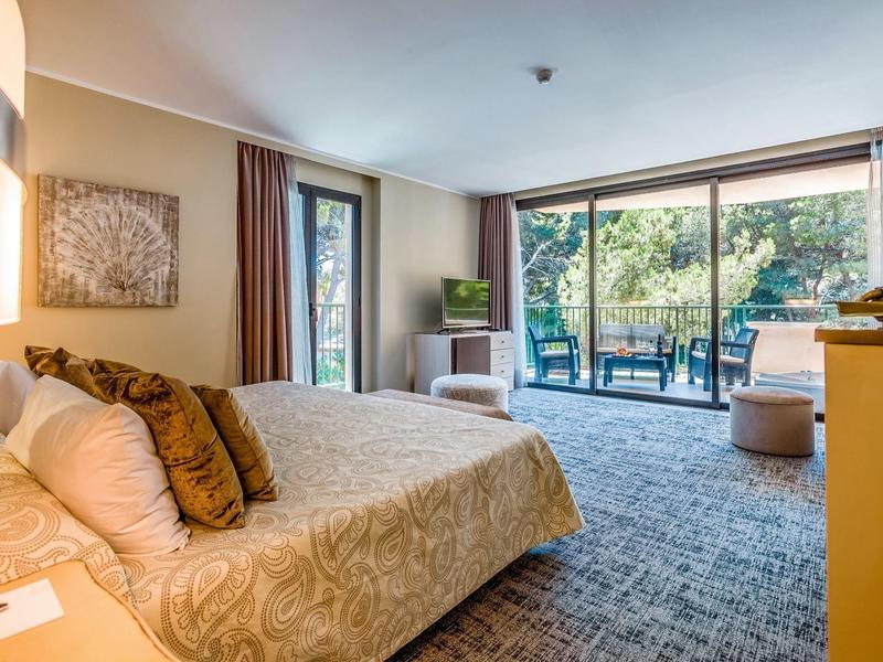 Cozy hotel room with large bed and balcony view of greenery.