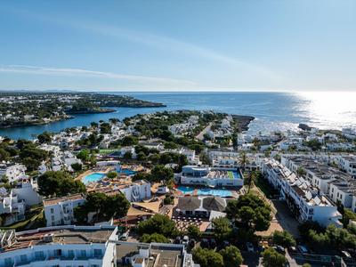 Vista aérea de una localidad costera con edificios blancos y mar azul al fondo.