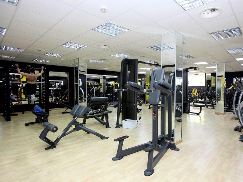Gimnasio moderno con diferentes equipos de entrenamiento y espejos en las paredes.