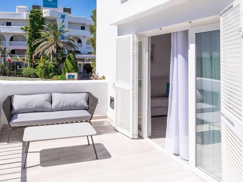 Terraza luminosa con sofá y mesa pequeña frente a puerta corrediza de hotel blanco.