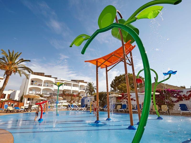 Área de juegos acuáticos con estructura de rocío en una piscina al aire libre de un hotel resort.