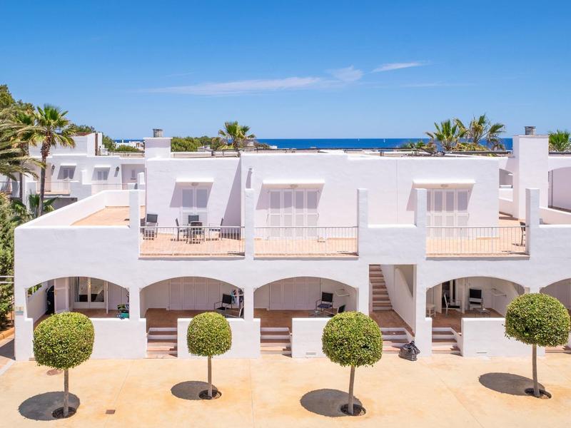 Moderna casa de vacaciones blanca con terraza soleada y vista al mar bajo cielo despejado.