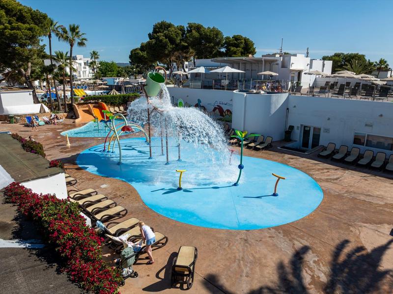 Área de juegos con pequeña piscina y juegos de agua junto a tumbonas en un jardín de hotel