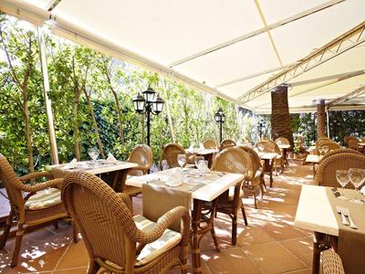 Terrassenrestaurant mit geflochtenen Stühlen und gedeckten Tischen unter Sonnensegeln.
