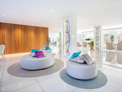 Moderner Hotel-Loungebereich mit weißen Sitzmöbeln, bunten Kissen und hellem, offenem Design.