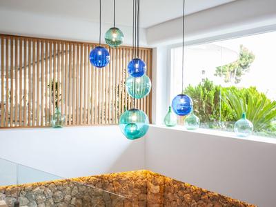 Mehrfarbige Glaslampen hängen über einem hellen, modernen Innenraum mit weißen Wänden und Holzlamellen.