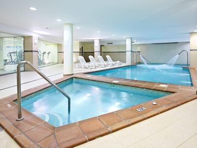 Innenpoolbereich mit zwei Becken, weißem Fliesenboden und mehreren weißen Liegestühlen.