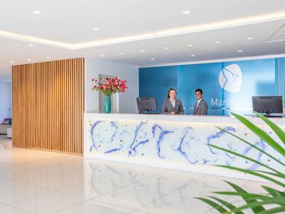 Moderner Empfangsbereich mit hellem Marmor-Tresen, blauem Wandlogo und zwei Empfangspersonen.