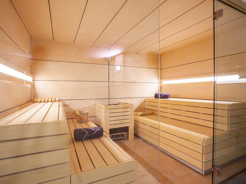 Helle Sauna mit Holzliegen, Wandspiegel und sanfter Beleuchtung an den Wänden.