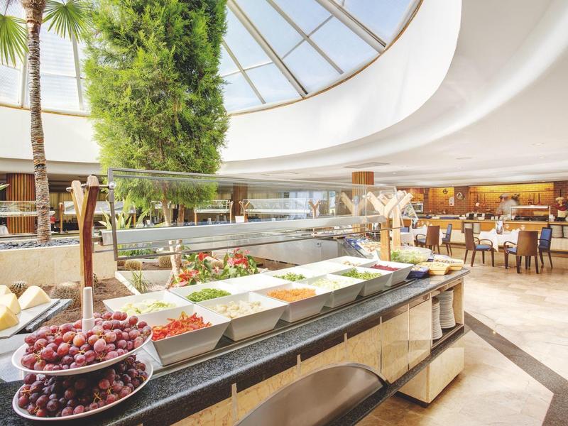 Großes helles Buffet mit Obst, Gemüse und Salaten in modernem Restaurant unter Glaskuppel.