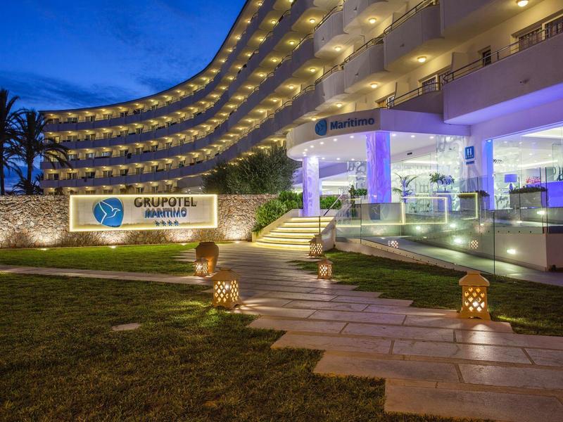 Modernes Hotelgebäude mit geschwungenen Balkonen, beleuchtetem Eingangsbereich und Weg mit Laternen.