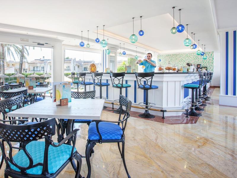 Helles, modernes Café mit blauen Stühlen, weißen Tischen und einer Bar im Hintergrund.