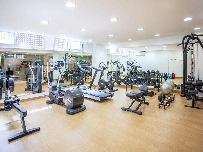 Heller Fitnessraum mit Holzfußboden, Spiegeln, Hanteln, Laufband und Kraftgeräten.