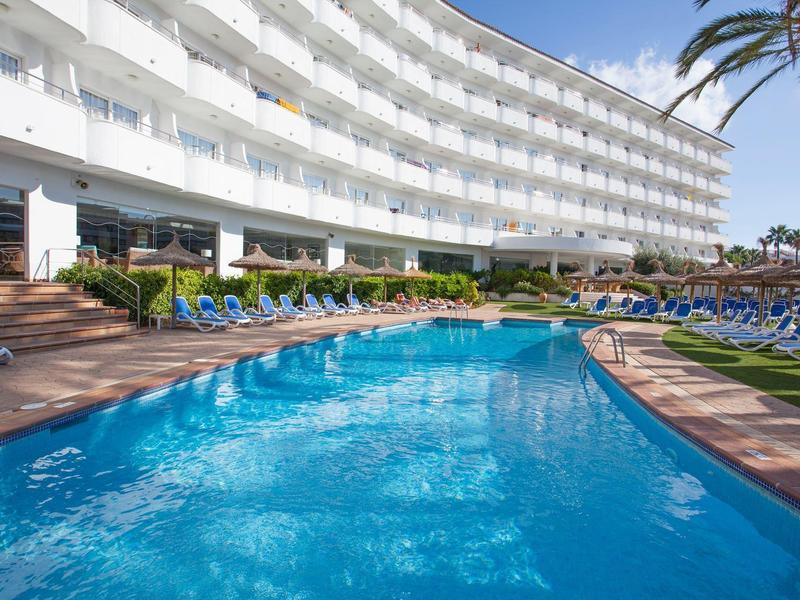Rundes weißes Hotel mit Sonnenterrasse und klarem blauen Pool unter blauem Himmel.