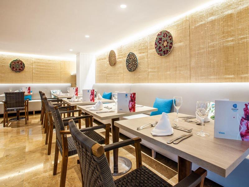 Modernes Restaurant mit Holztischen, geflochtenen Stühlen und dekorativen Wandornamenten aus Holz.