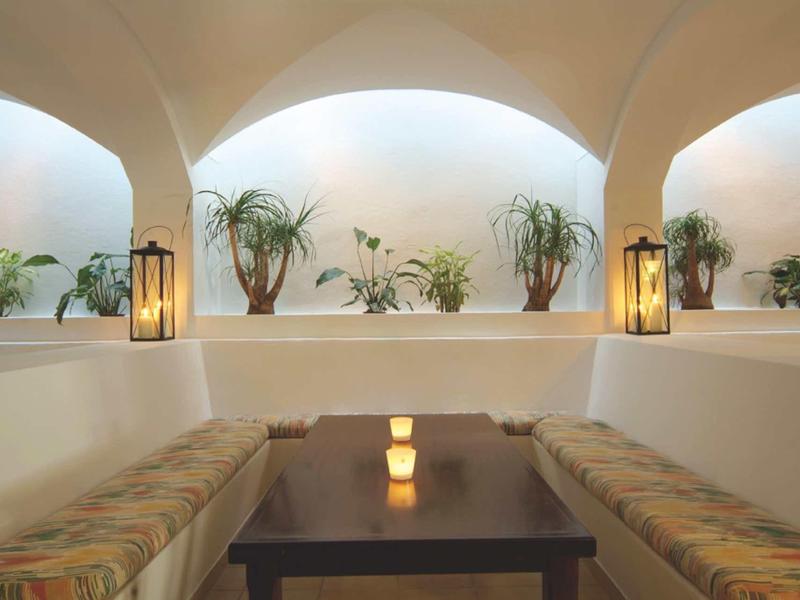 Cozy seating area with cushions, plants, and lanterns in a bright, arched room.