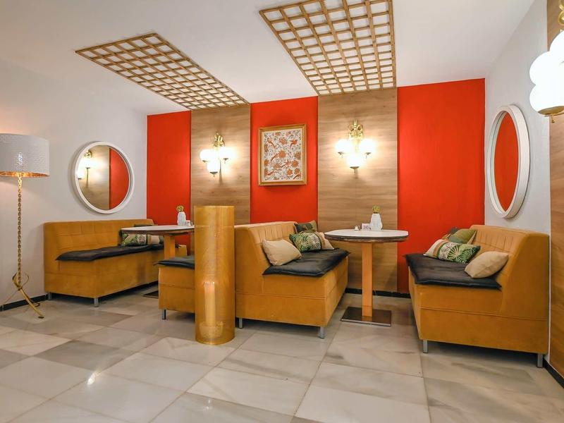 Modern hotel interior with brown seating booths, red walls, and round mirrors.
