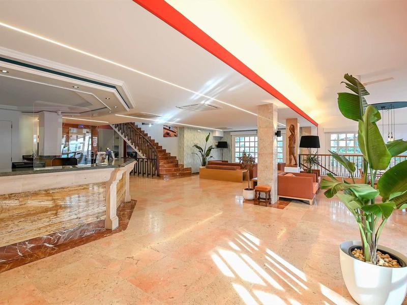 Bright hotel lobby with marble reception desk, seating area, and large potted plant.